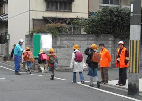 工事現場で登校中の子どもたちに声をかける現場警備員の写真