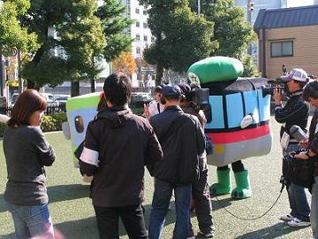 撮影スタッフに囲まれる，着ぐるみの「京ちゃん」と「都くん」