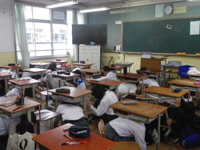 避難訓練において机の下に身を隠している写真