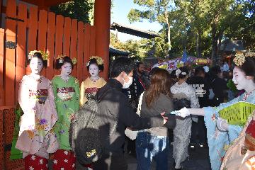 楼門を潜る市民に舞妓さんがティッシュを手渡します