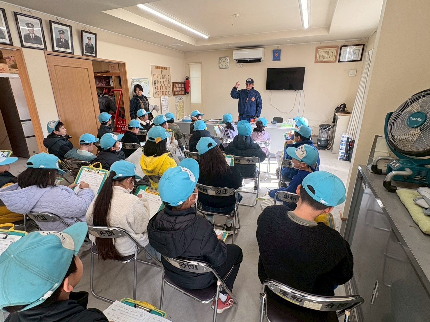 消防分団の器具庫で小学生が資器材説明を受けている様子。