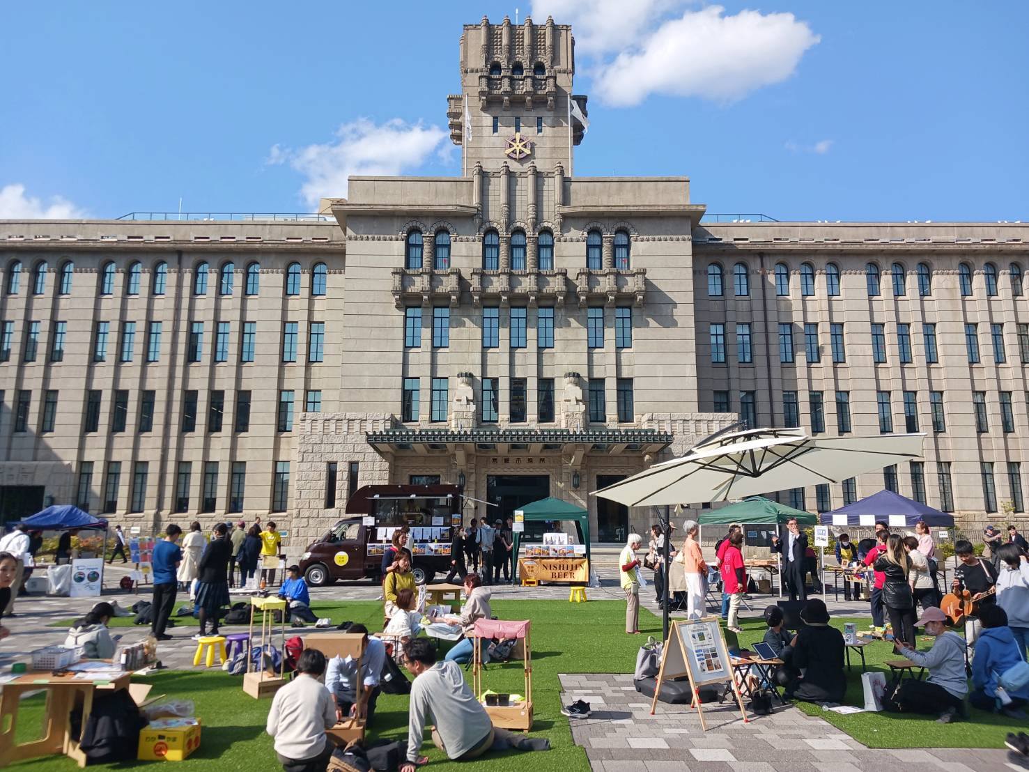 市役所庁舎前広場で開催されている「小さな芝生広場」を見学しました。 今回は、日本新薬株式会社の移動図書館「きらきら未来号」や福祉とビールが融合した「フクシのビール」の販売にも来ていただき、多くの方が楽しんでおられました。