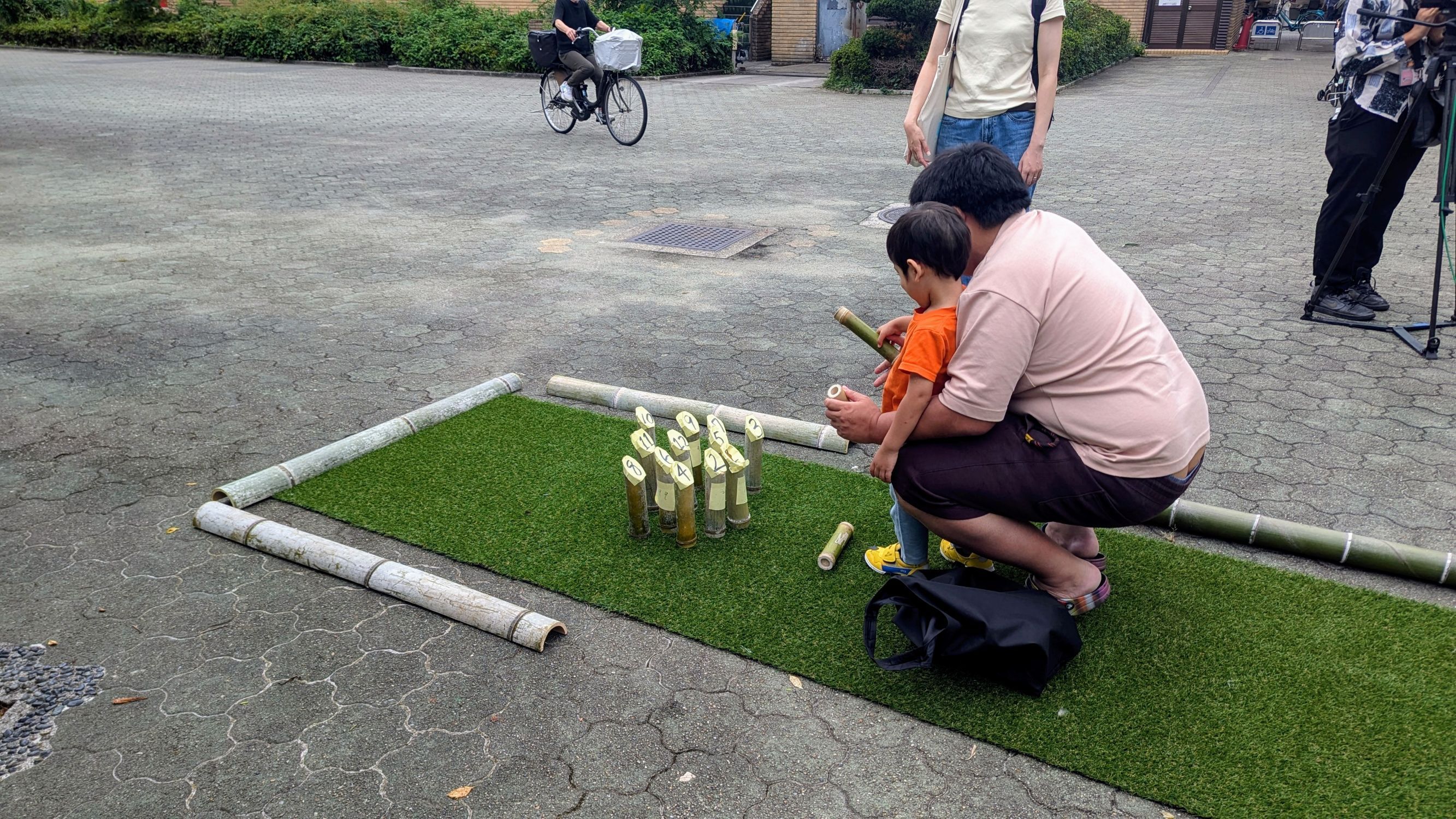 通りすがりの親子が竹で出来たモルックで遊んでいる状況の写真